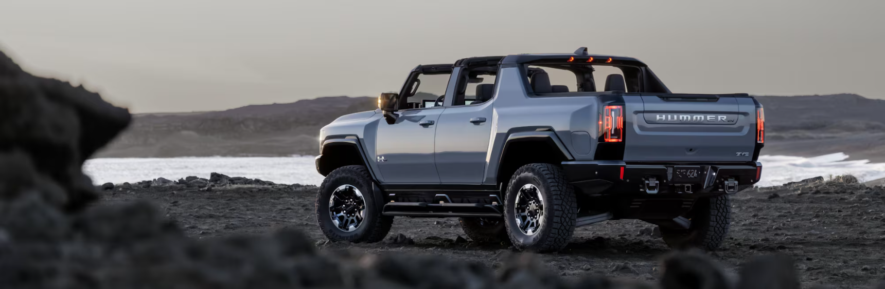 Back view of 2026 GMC Hummer EV pickup on rocky terrain at sunset.