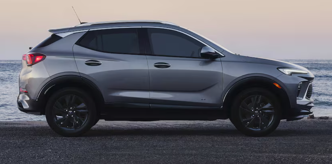 Side profile of a gray Buick Encore GX SUV parked near the ocean with waves in the background at dusk.