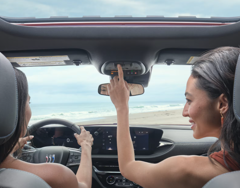 The interior of a 2026 Buick Envista with passengers enjoying an open sunroof by the beach.